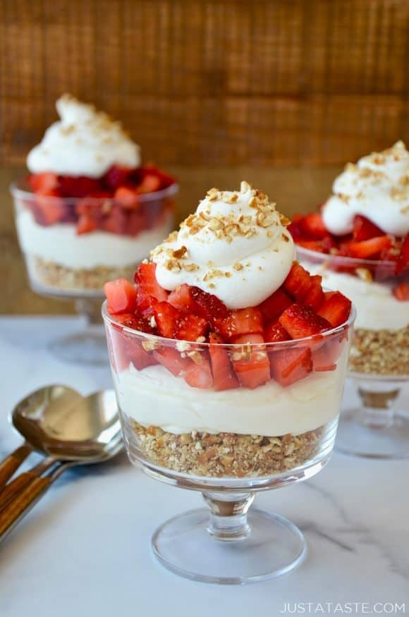 three desserts with strawberries and whipped cream in small glass dishes on a table