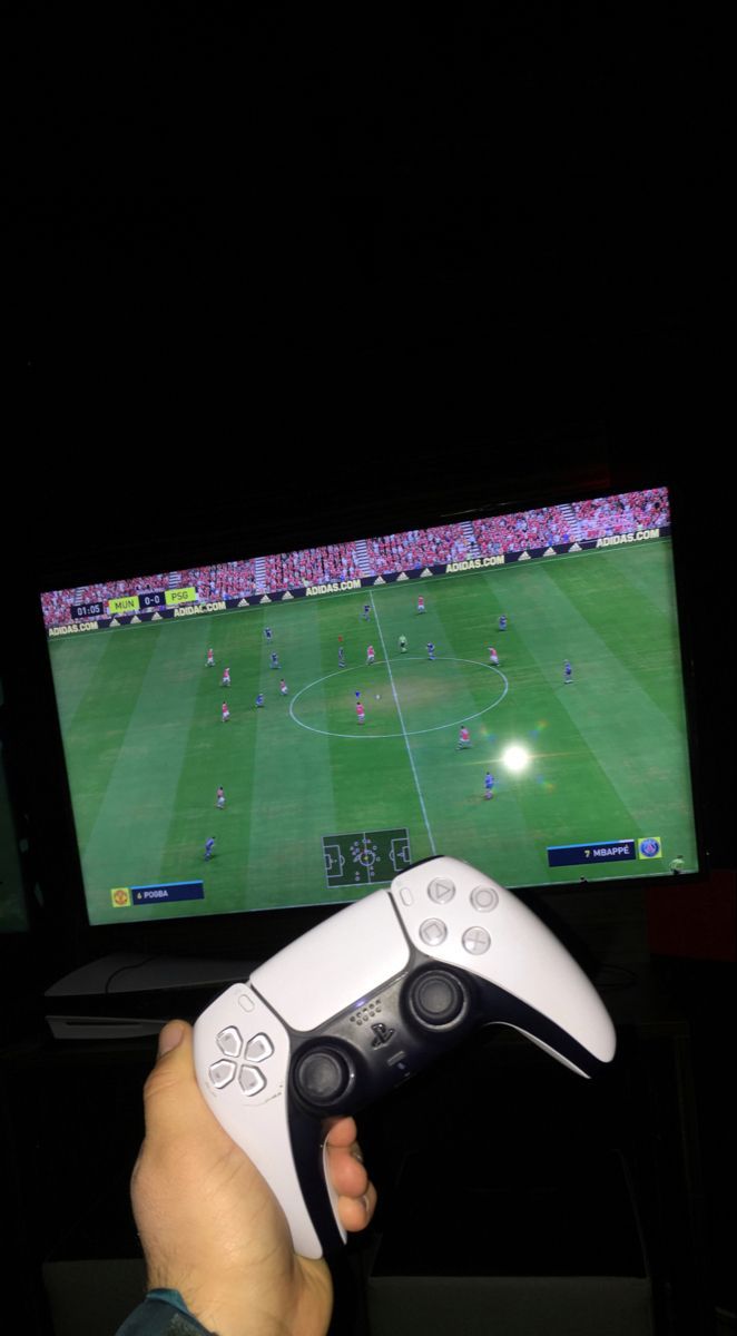 a person holding a video game controller in front of a flat screen tv at night