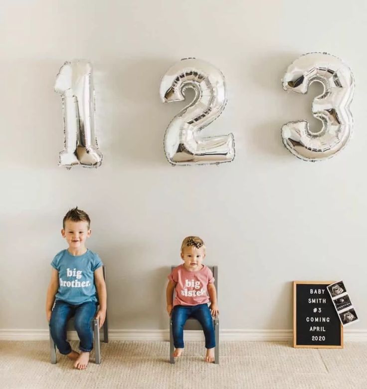 two children sitting on chairs in front of balloons that spell out the number twenty three