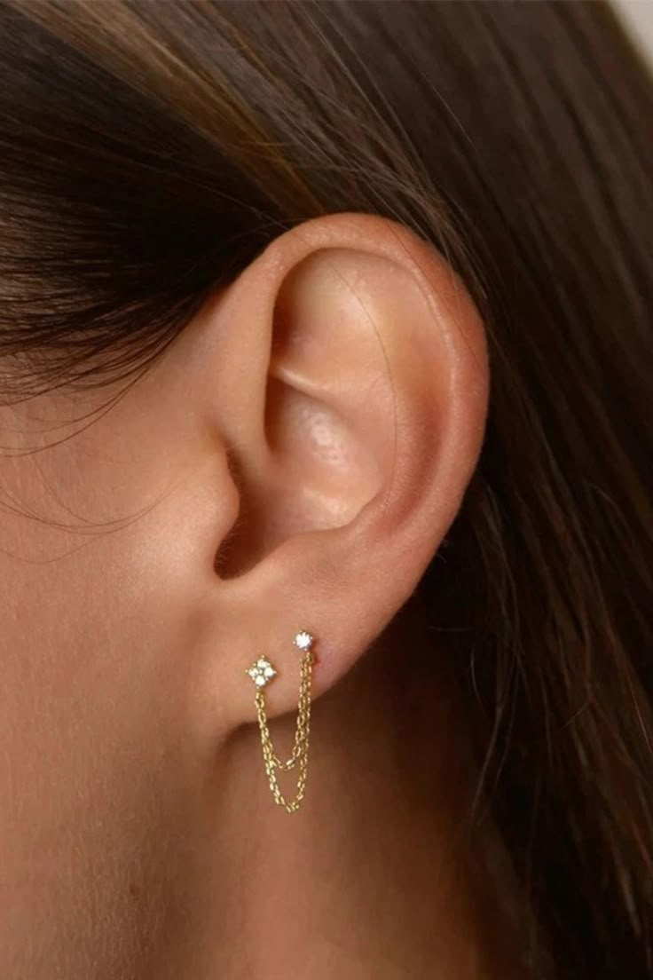 A woman wearing a double stud chain earring. Earrings For Two Piercings Dainty, Double Piercing Studs Classy, Second Ear Piercing Cuff, Small Earring Chain, Double Ear Piercing Top, Earrings 2 Holesstud, Silver Earrings Two Holes Stud, Cheap Pierced Summer Earrings, Trendy Affordable Piercings As Gift