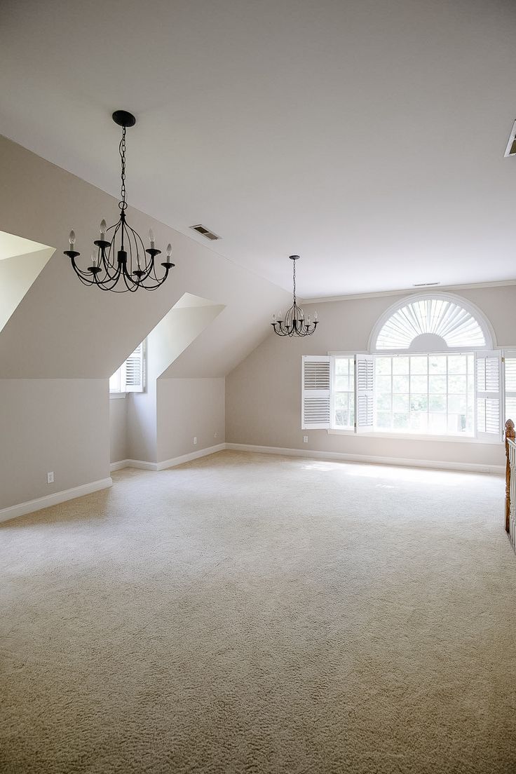 an empty living room with chandelier and large carpeted area in the middle