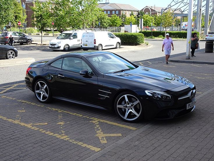 a black sports car parked in a parking lot next to some buildings and people walking on the sidewalk