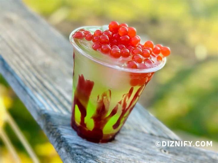 a plastic cup filled with berries sitting on top of a wooden bench