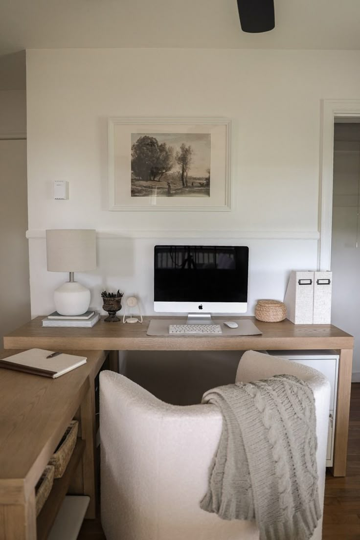 a desk with a computer on top of it next to a white chair and lamp