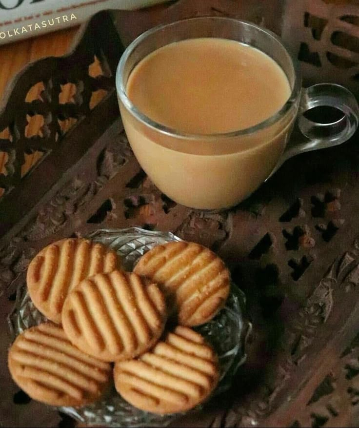 some cookies are on a glass plate next to a cup of coffee and a book