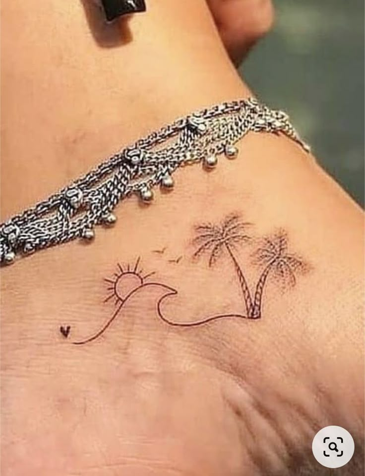 a woman's foot with a small tattoo on the ankle and palm trees in the background