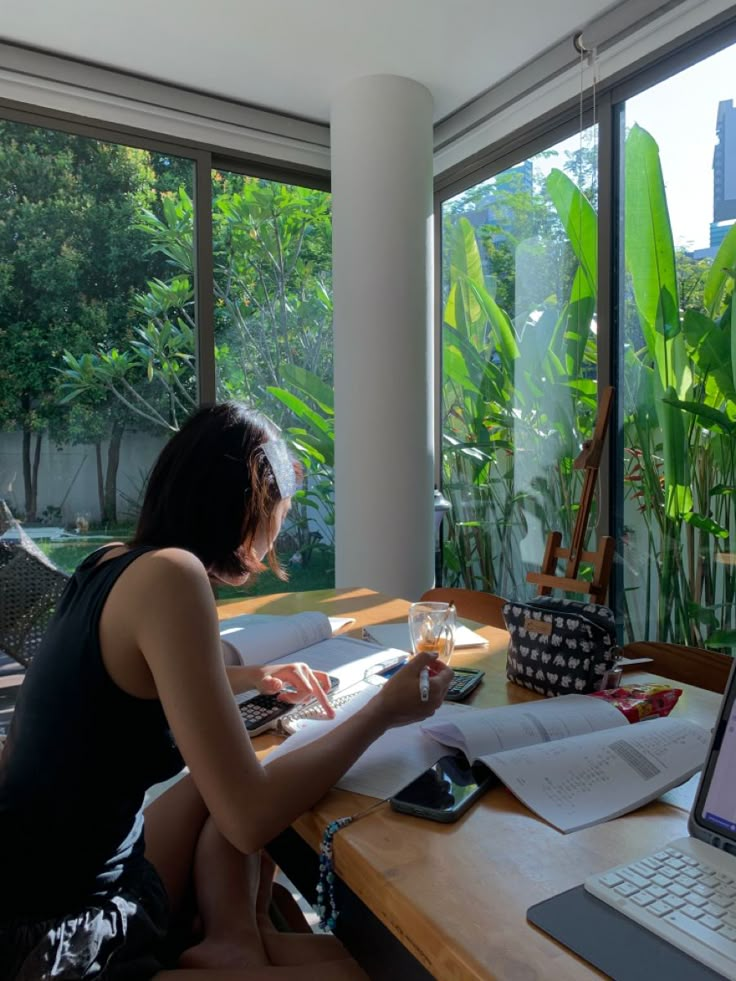 a woman sitting at a desk in front of a laptop computer looking out the window