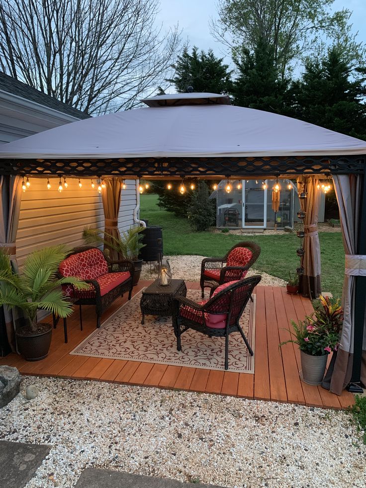 a patio covered with furniture and lights on the side of a house in front of some trees