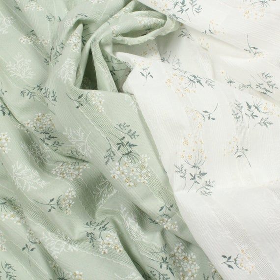 two white and green fabric with small flowers on the top one is folded up in half