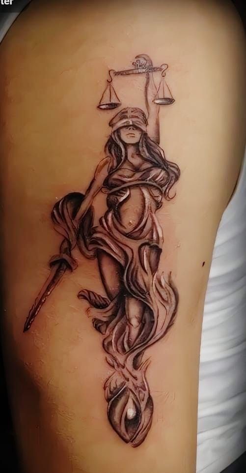 a lady justice tattoo on the back of a woman's thigh, with scales in the background