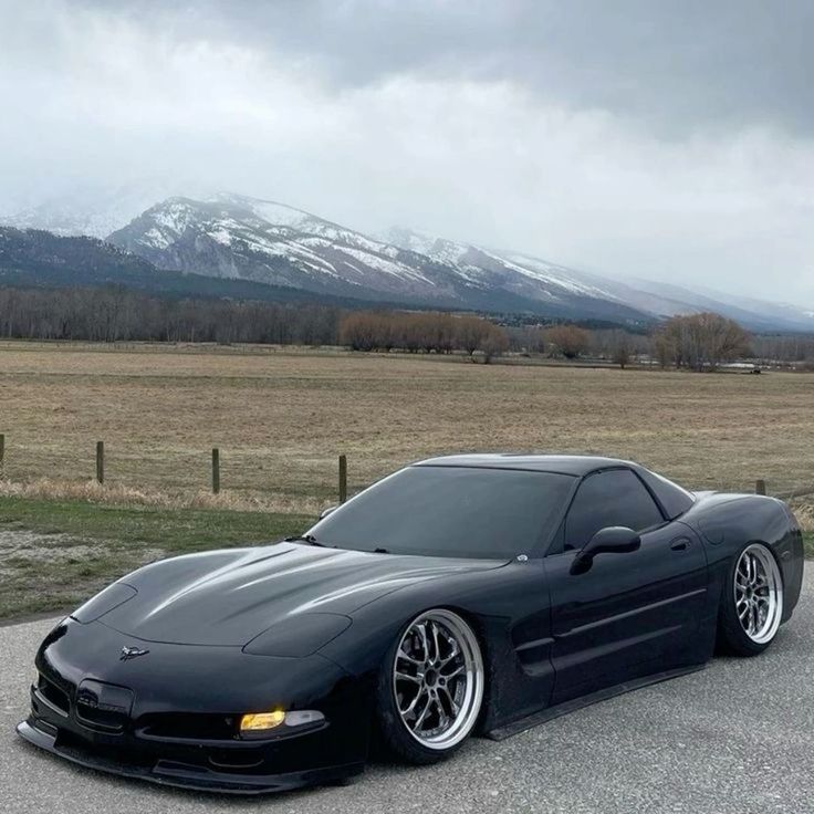 the black sports car is parked on the side of the road in front of mountains