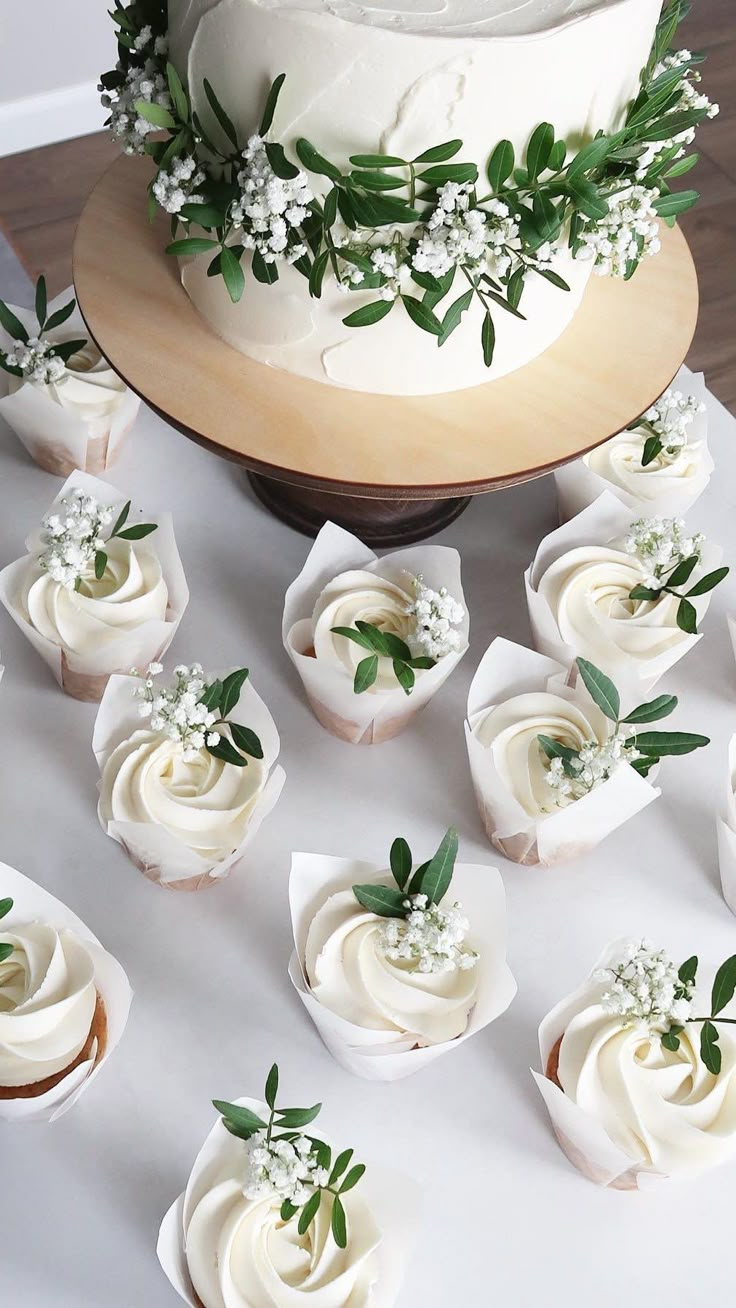 there are many cupcakes on the table with white frosting and greenery