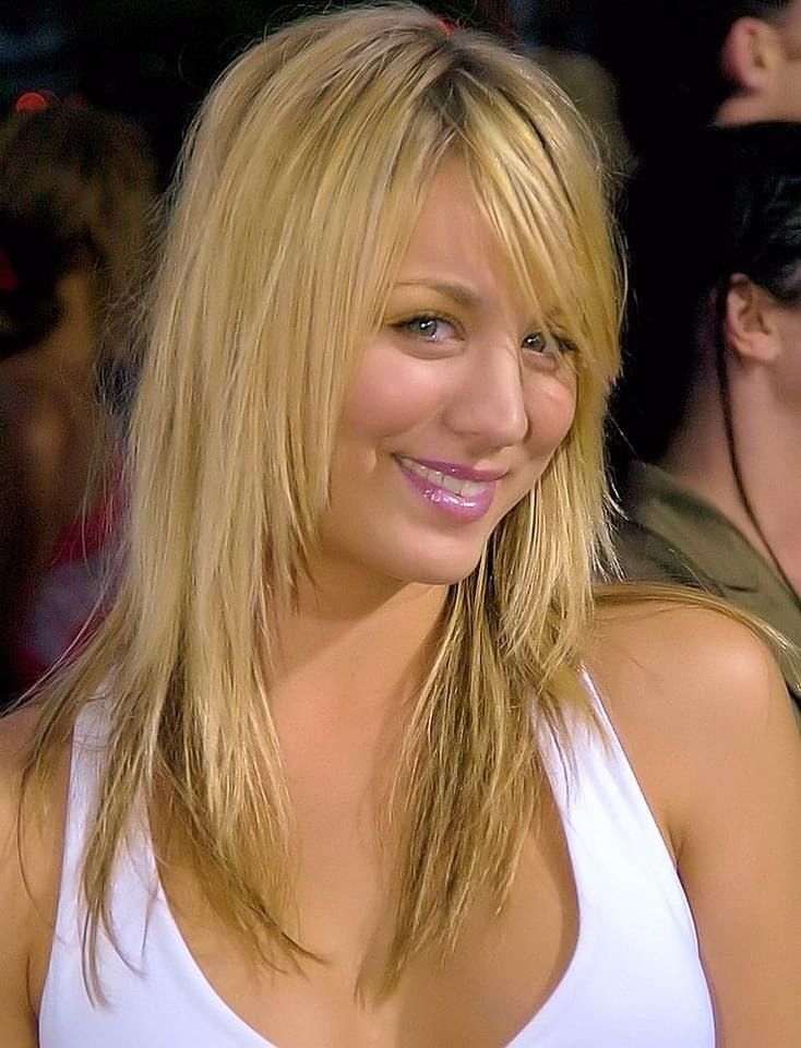 a woman with long blonde hair and blue eyes smiles at the camera while wearing a white tank top