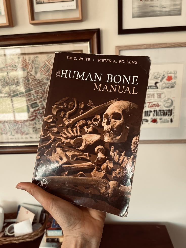 the human bone manual is held up in front of a wall with pictures on it