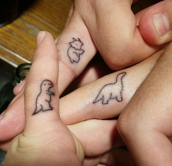 two people holding hands with tattoos on their fingers and one has a small dog in the middle