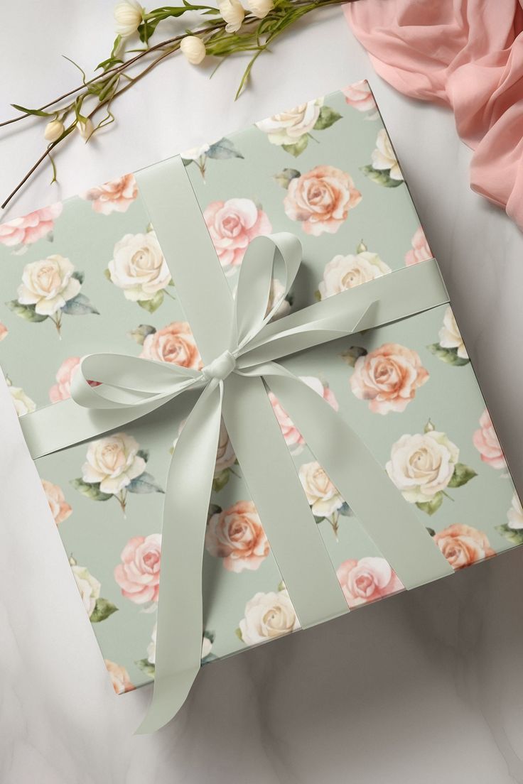 an open gift box with a bow on it next to pink flowers and greenery