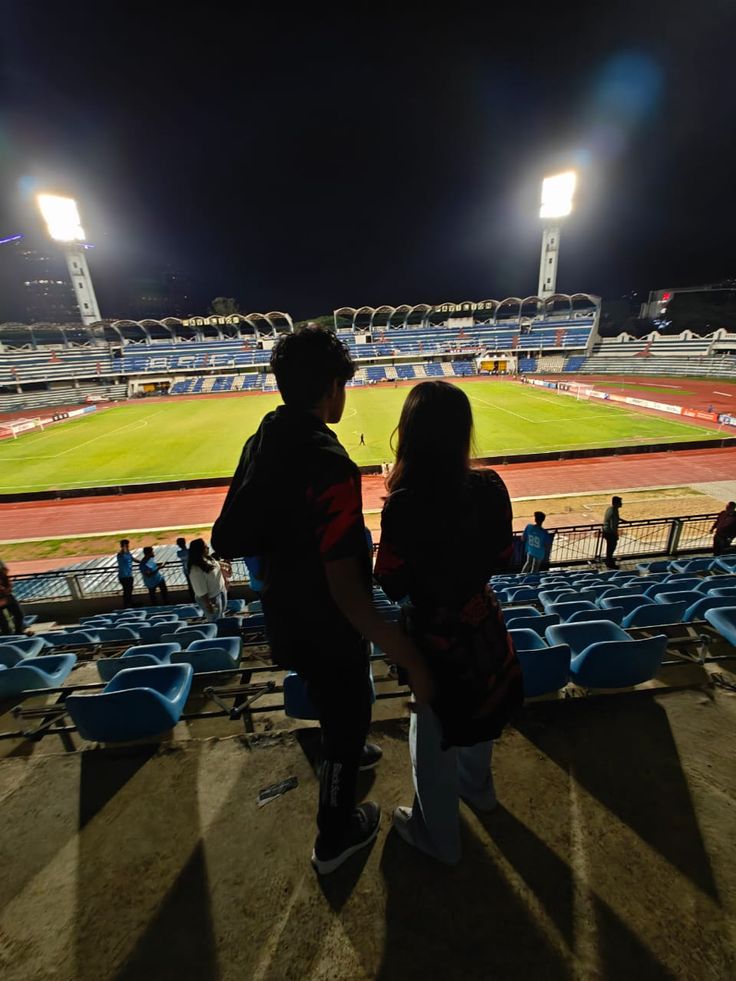 two people standing at the end of a baseball field looking out into an empty stadium