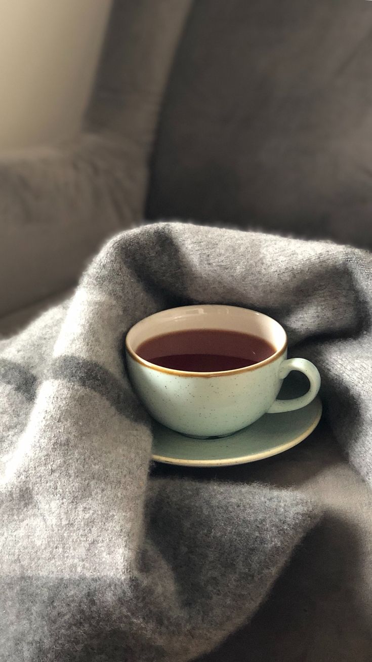 a cup of tea sits on a saucer with a gray blanket draped over it