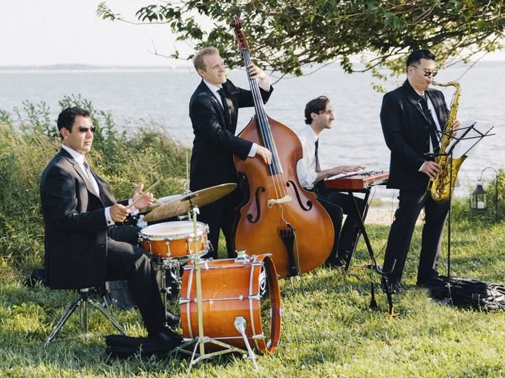 a group of men playing instruments on top of a grass covered field next to the ocean