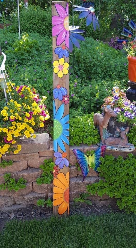 a wooden pole with flowers painted on it in the middle of a flower garden area