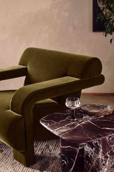 a green chair sitting on top of a marble coffee table next to a glass vase