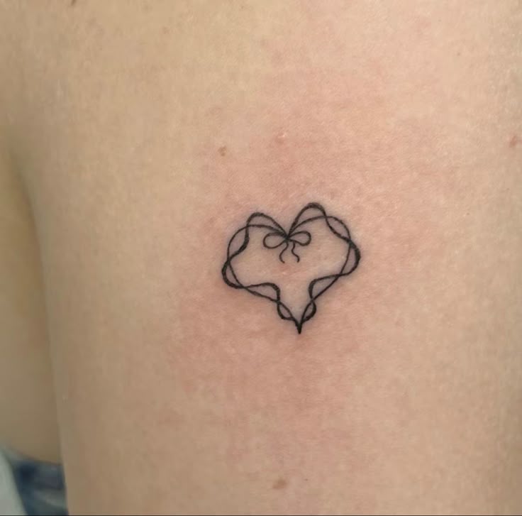 a small heart tattoo on the back of a woman's left thigh, with a bow