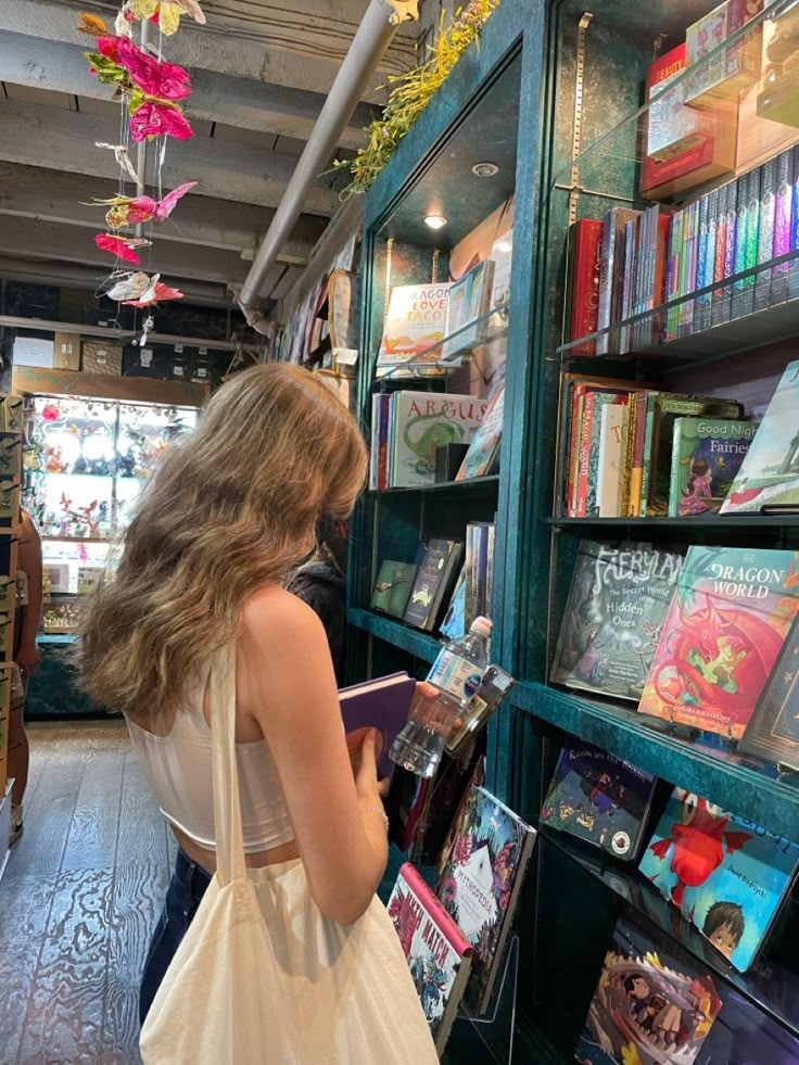 a woman in a white dress looking at books on shelves with flowers hanging from the ceiling