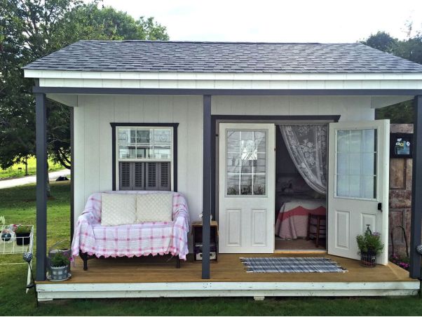 a small white shed with a couch on the porch