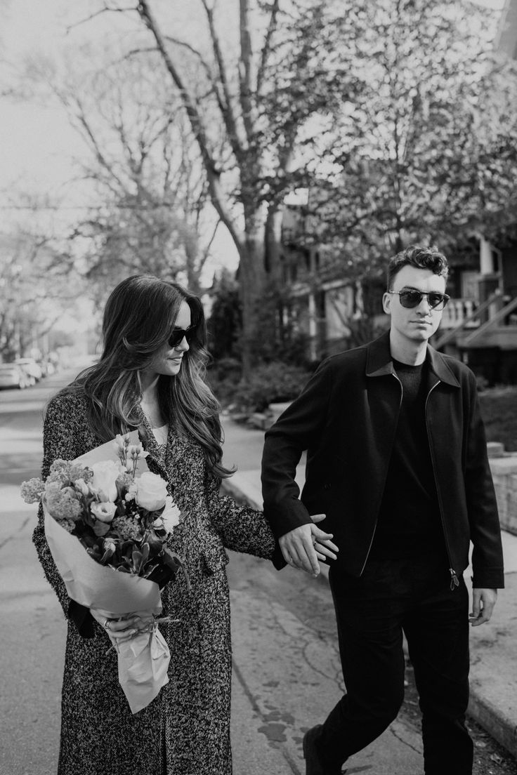 Black and white photo of a couple holding hands walking down a sidewalk in a city residential neighbourhood. She is holding a large bouquet of flowers. Toronto Neighbourhoods, A Bouquet Of Flowers, Enduring Love, Romantic Moments, Toronto Wedding, Captured Moments, Human Connection, Bouquet Of Flowers, Engagement Anniversary