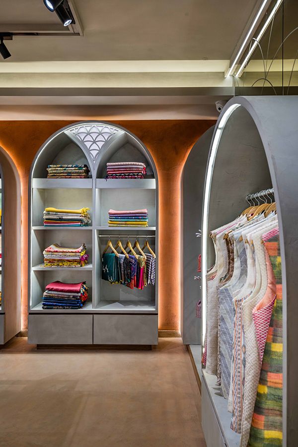 the inside of a clothing store with lots of clothes on shelves and in front of an arched doorway