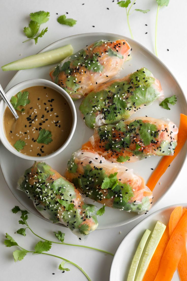 a white plate topped with sushi rolls next to a bowl of dipping sauce and carrots