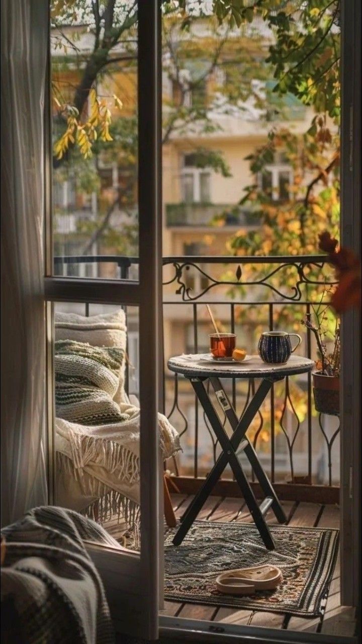 an open balcony door with a table and chairs on it, looking out onto the street