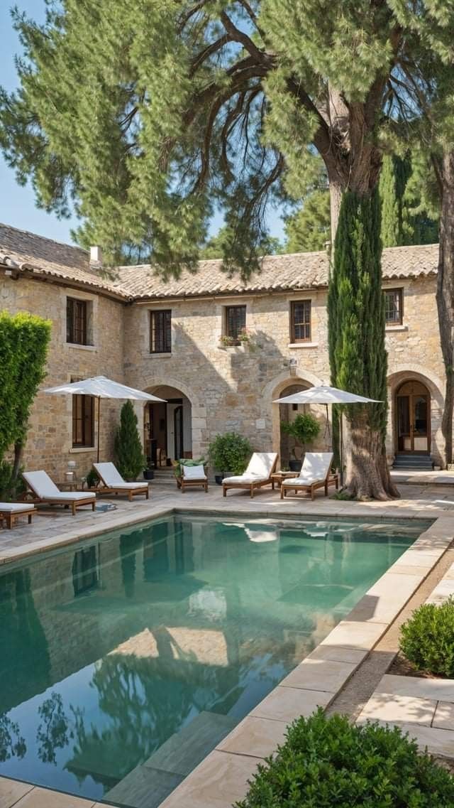 an outdoor swimming pool with chaise lounges and umbrellas in front of a stone house