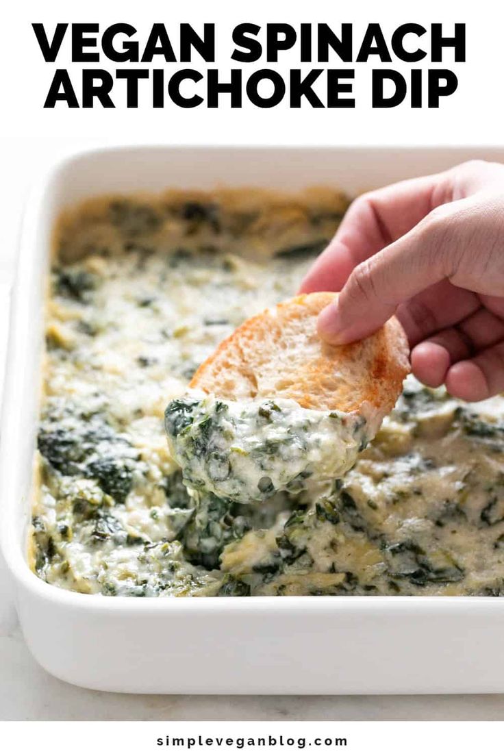 spinach artichoke dip in a white bowl with a hand dipping it into the dip