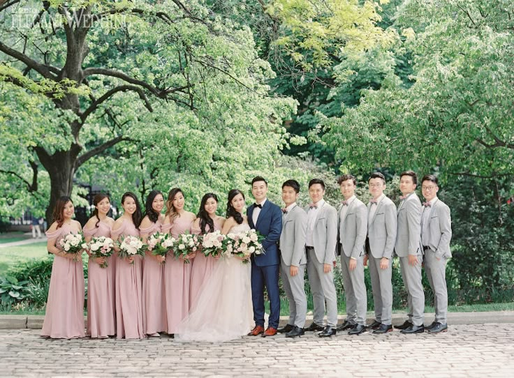 a group of people standing next to each other in front of trees and bushes with flowers