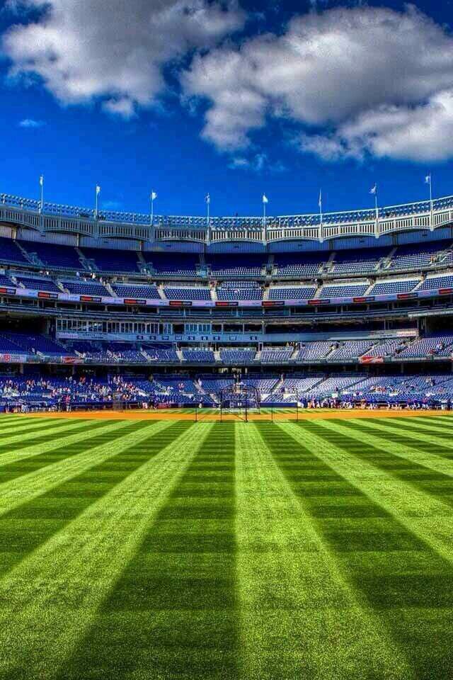 an empty baseball stadium filled with lots of green grass and blue skies in the background