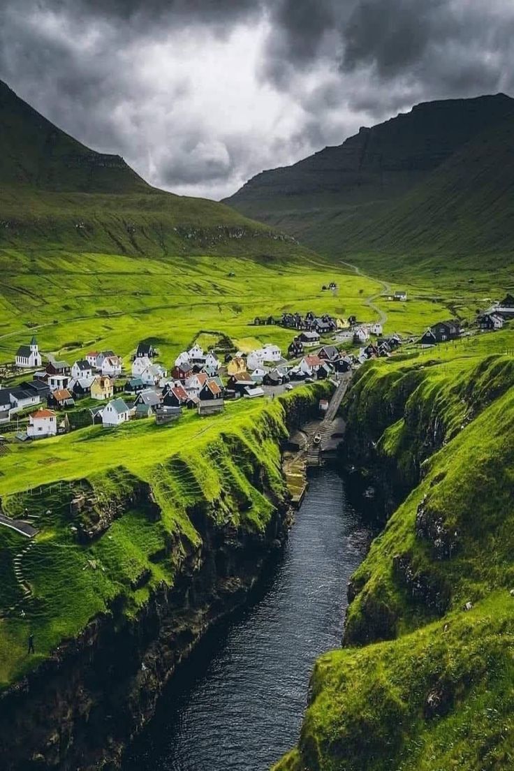 a small village on the side of a green hill with a river running through it