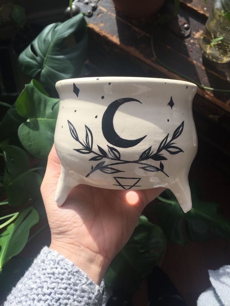 a hand holding a white ceramic bowl with a crescent and leaves design on the side