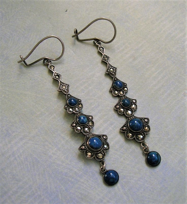 a pair of silver and blue earrings on a white tablecloth with a black beaded earring