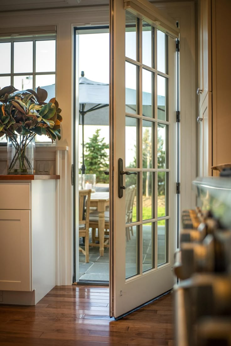 an open glass door leading to a kitchen and dining room with wooden floors, white walls and cabinets