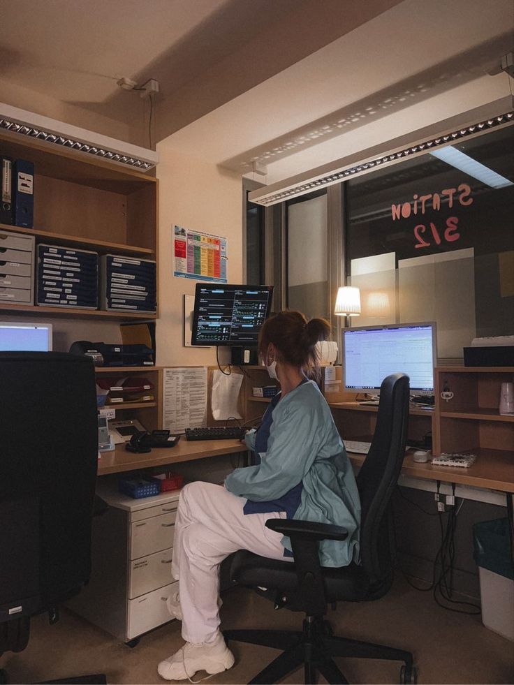 a woman sitting at a desk in front of two computer monitors and a desktop monitor