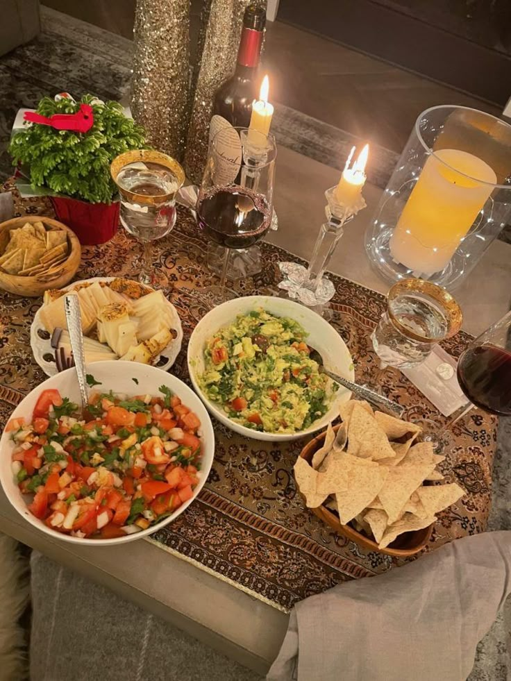 a table topped with bowls of food next to glasses of wine and plates of chips