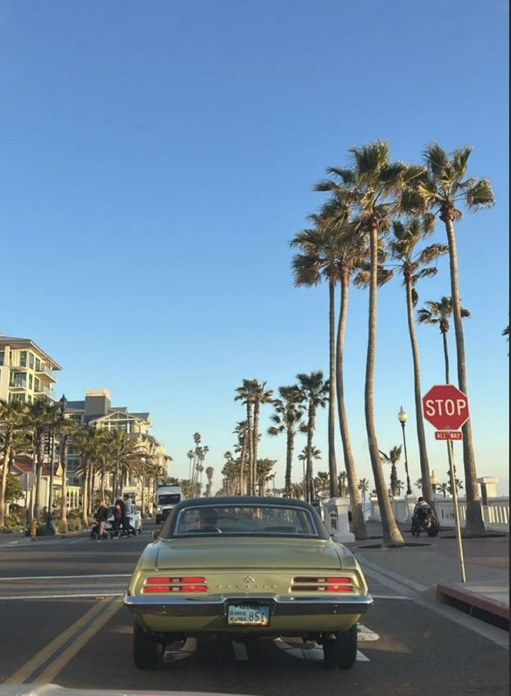 an old car is parked on the side of the road in front of palm trees