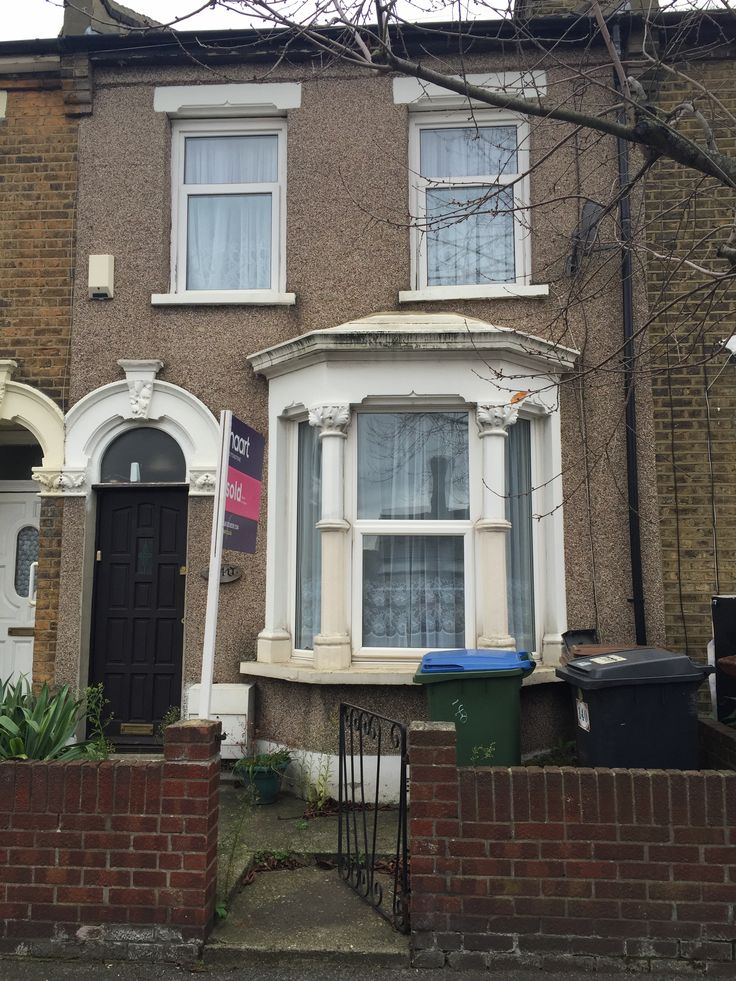 a brick house with white trim on the front door and windows, next to a fence