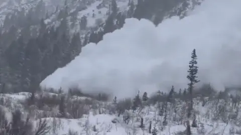 A huge white plume of snow barrels down a mountain.