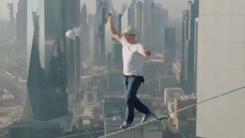 Man balancing on highline with Dubai skyline in the background