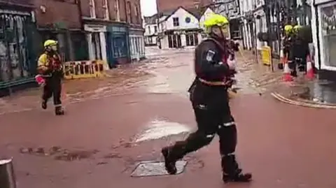 Emergency services workers run from approaching flood waters on street in Tenbury Wells