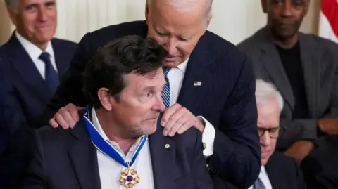 Michael J Fox wearing the Medal of Freedom with Joe Biden behind him holding his shoulders