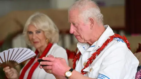 King Charles holding a black cup next to Queen Camilla