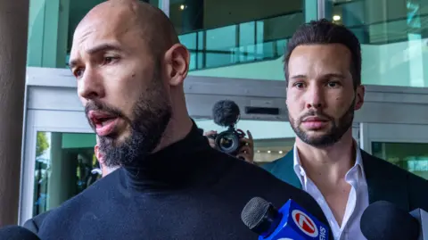 Andrew Tate and his brother Tristan at Fort Lauderdale Airport in Florida with media pointing microphones at them for comment